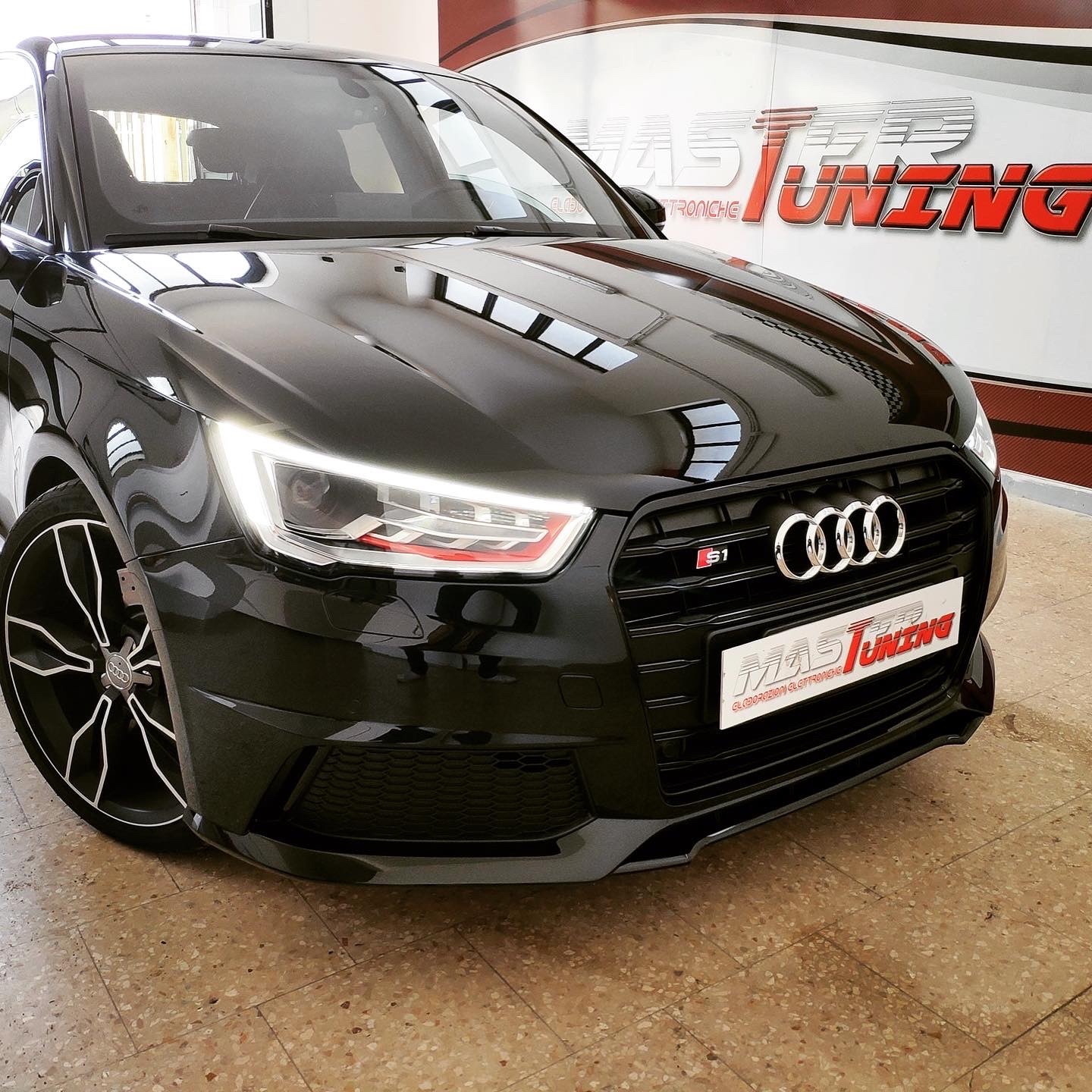 Audi S1 nera vista anteriore con fari LED accesi e logo S1 sulla calandra, in officina MasterTuning