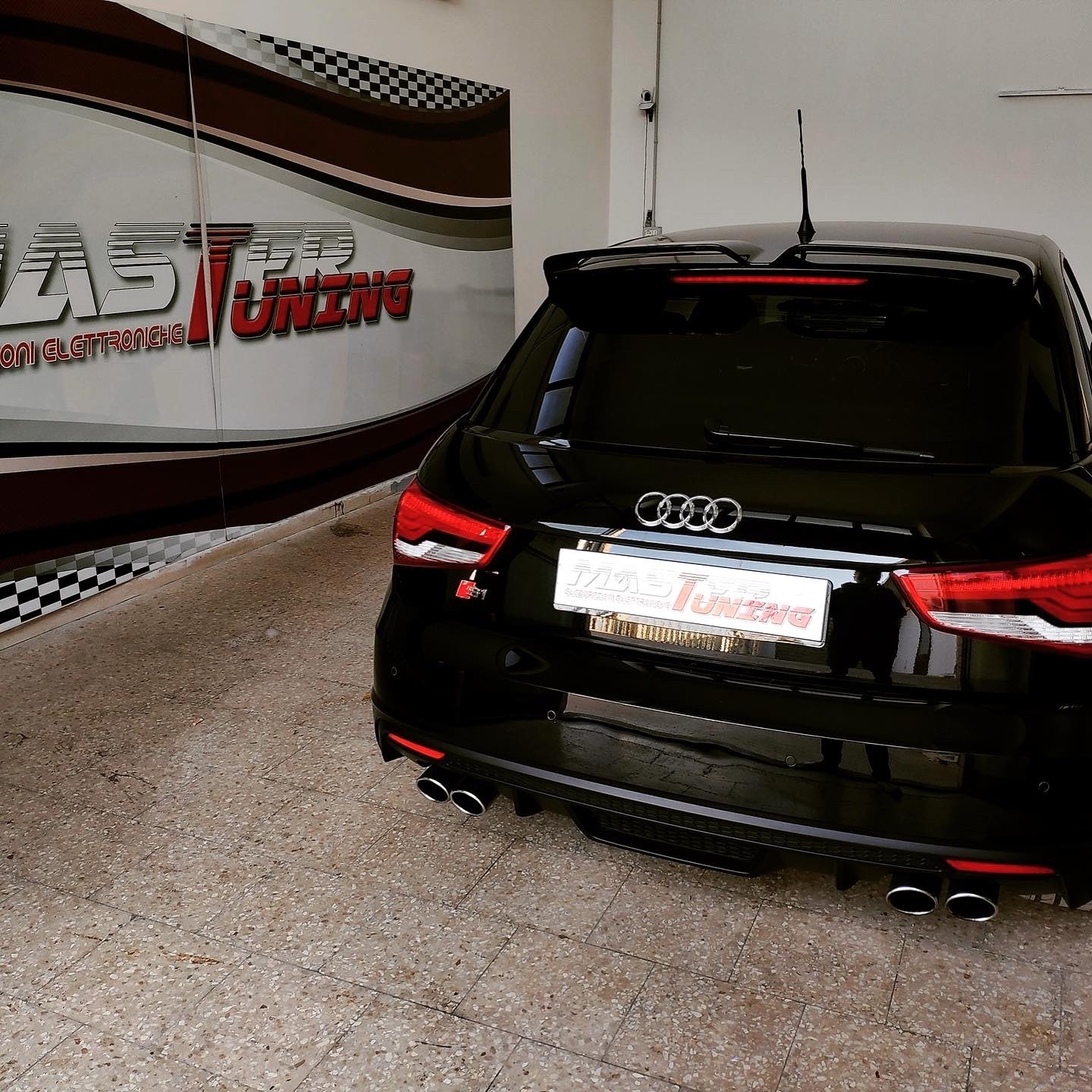 Audi S1 nera vista posteriore con quattro terminali di scarico e spoiler, davanti all'insegna MasterTuning