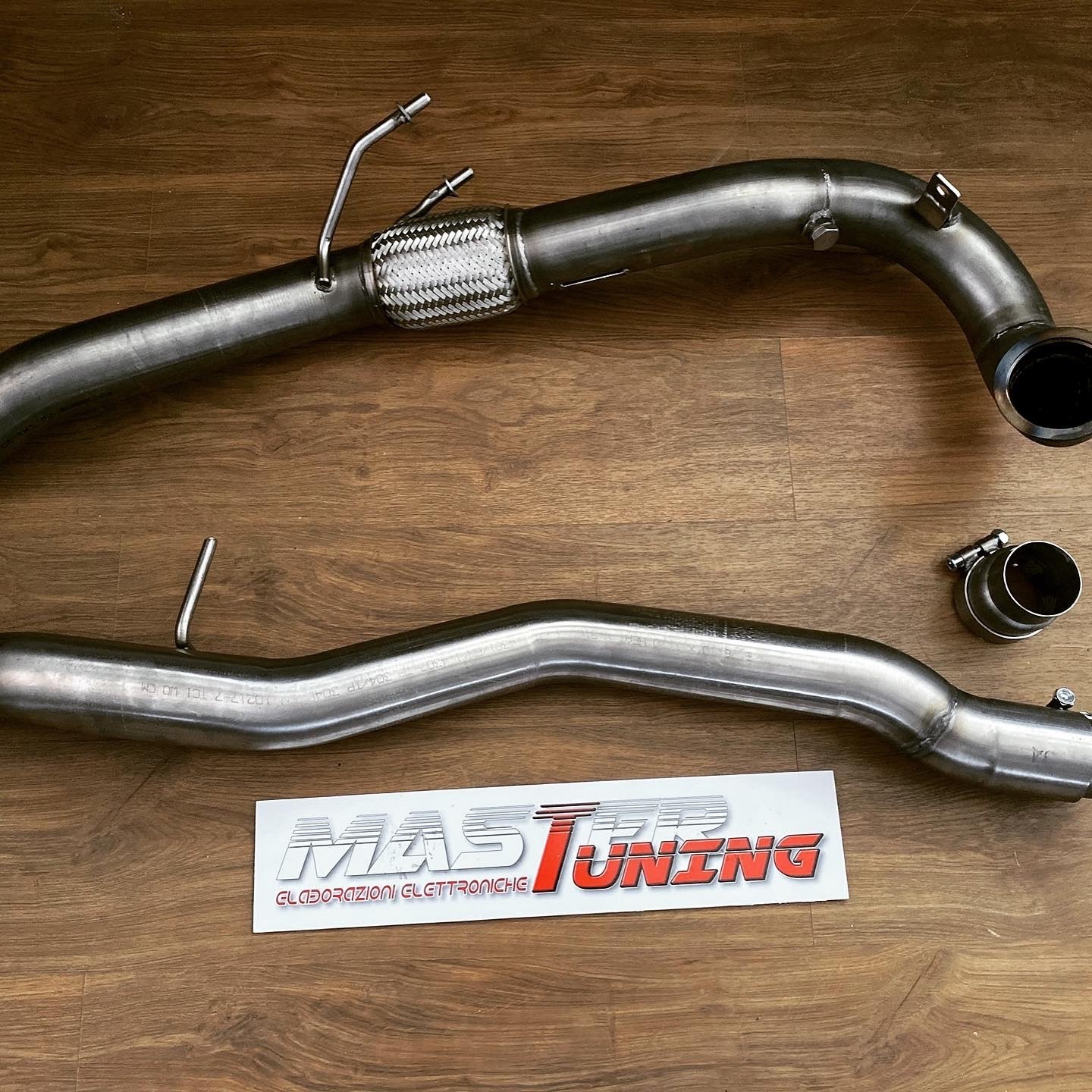 Downpipe e tubo di scarico in acciaio inox per Audi S1 appoggiati su un pavimento in legno